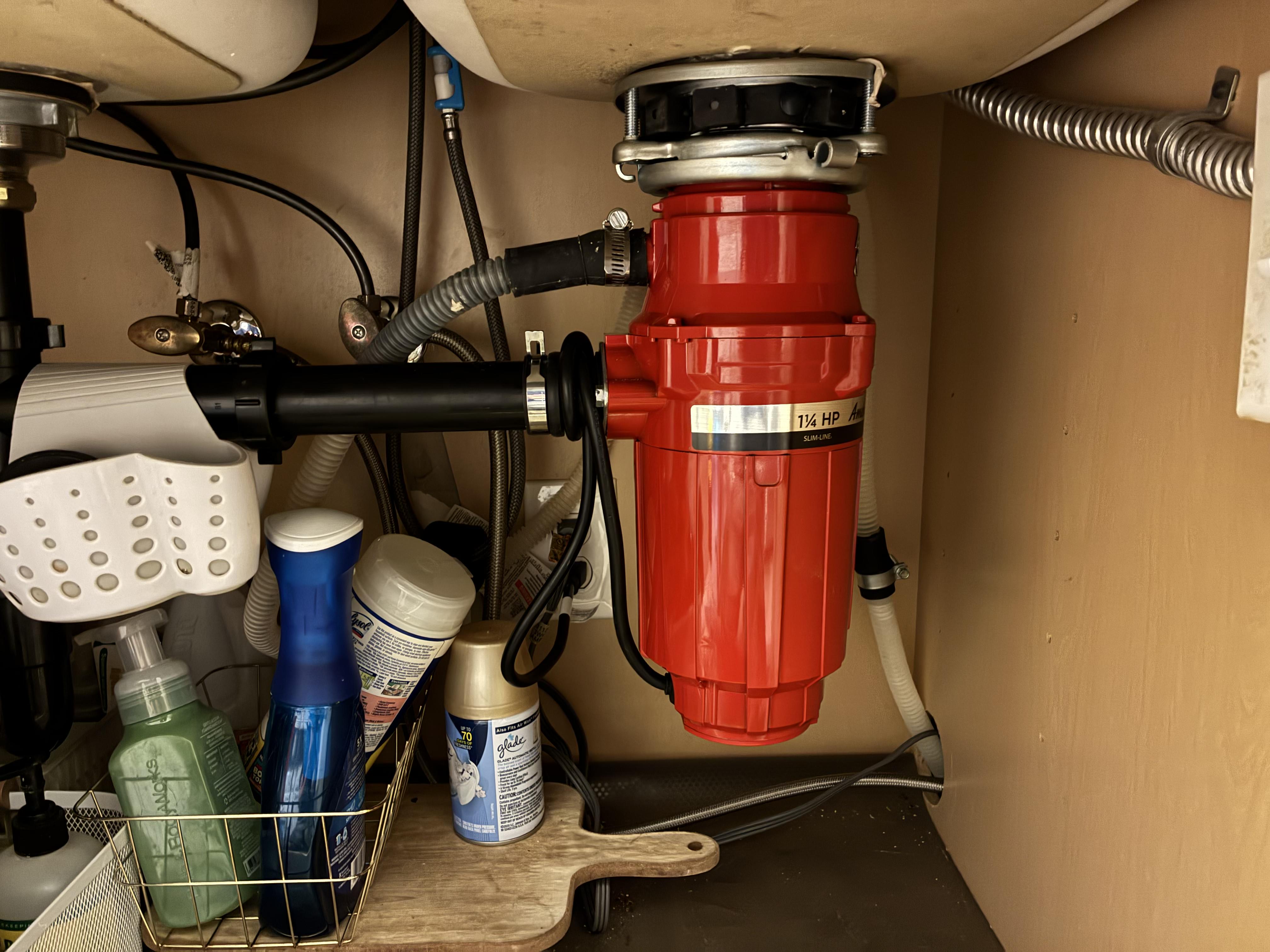 Technician replacing a garbage disposal under a kitchen sink